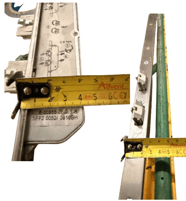 A close-up of a metal rail or track component with a yellow measuring tape laid across it to show dimensions. The product appears to be a long silver metal track or guide rail with small hardware and a green strip along one side.